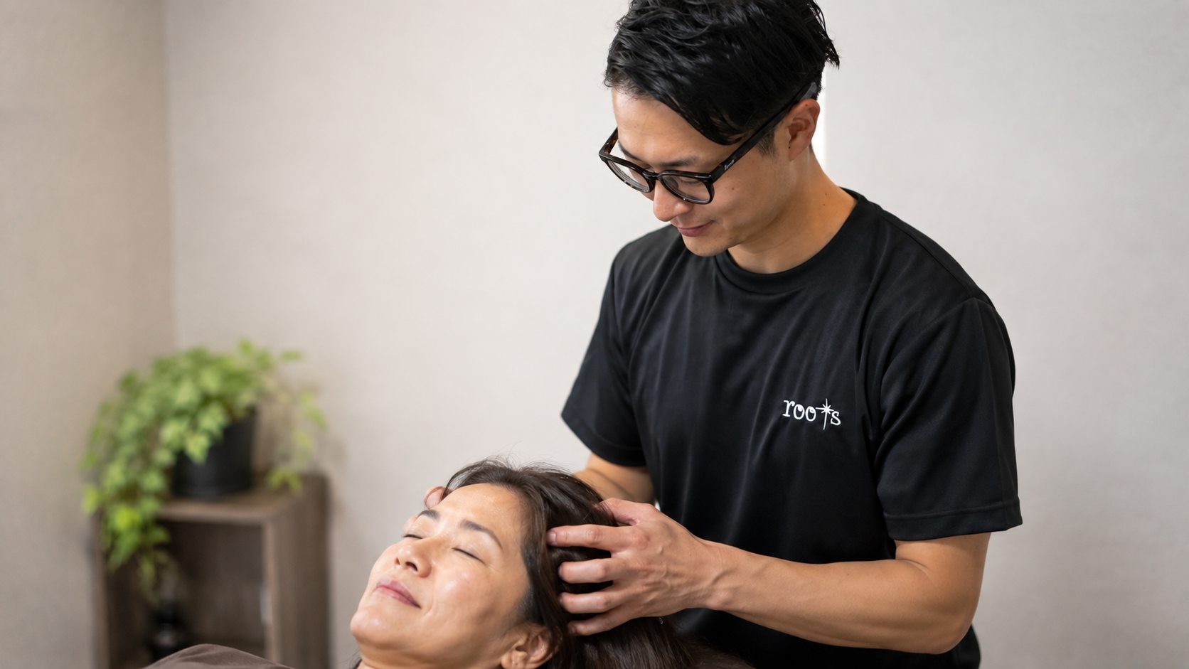 ベッドに仰向けになった女性の頭に手をあて、ヘッドケアを行うトレーナー