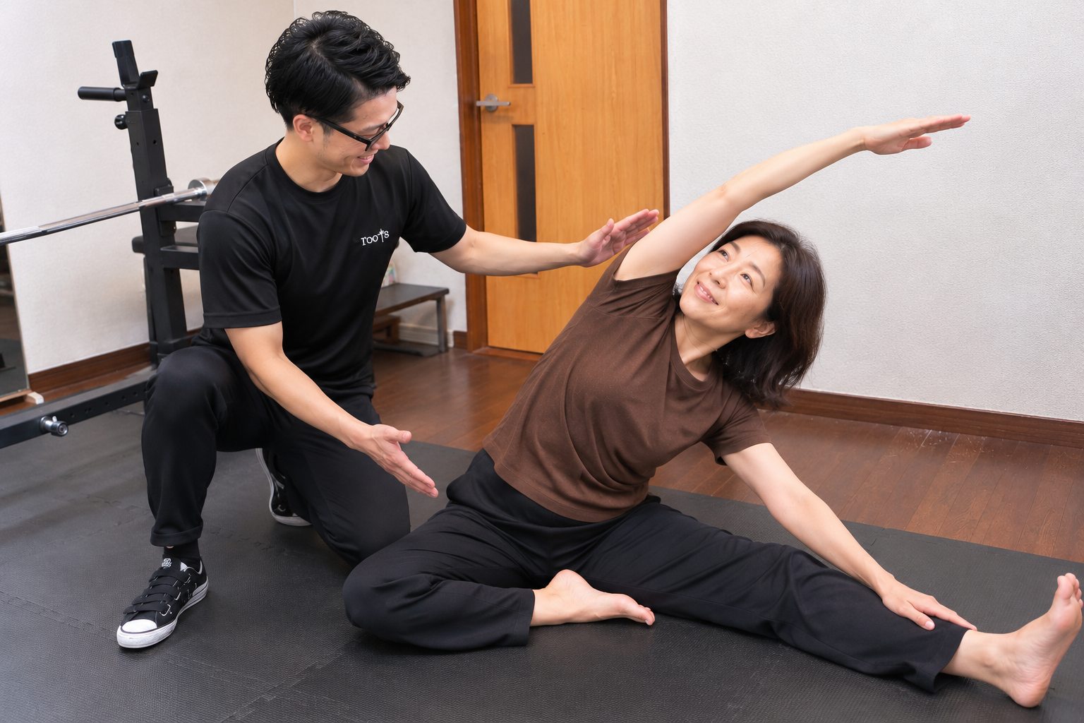 福井市のボディメイクスタジオrootsで、トレーナーの補助を受けて体側を伸ばす50代女性